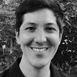 A white person with brown hair smiling at the camera wearing a dark colored polo shirt